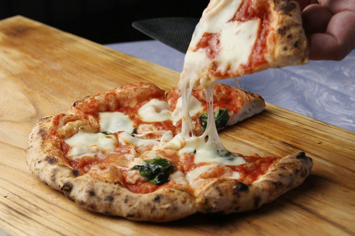 A slice of pizza being lifted from a wooden board, cheese stretching