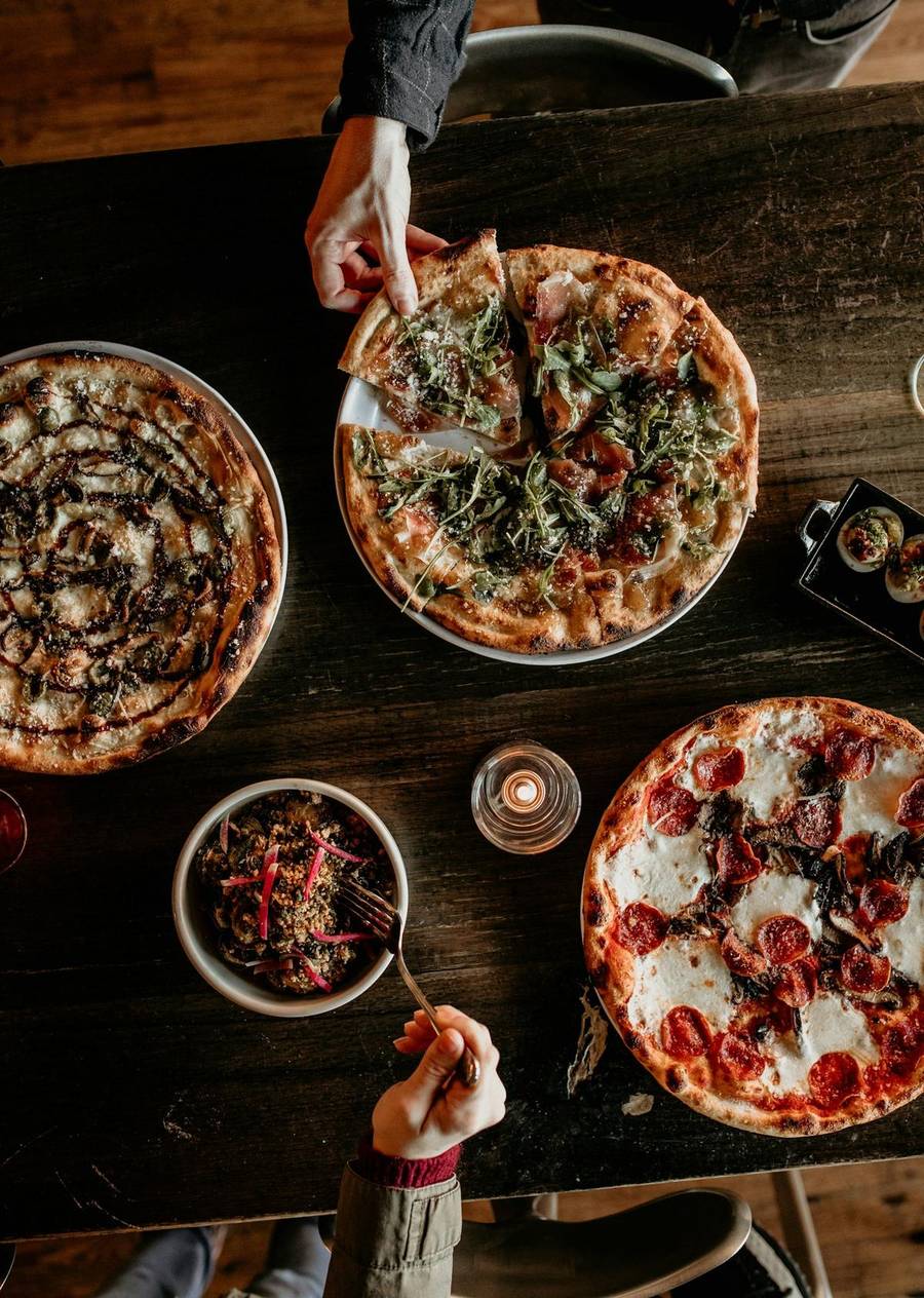 Several pizzas and sides spread across a dark wooden table